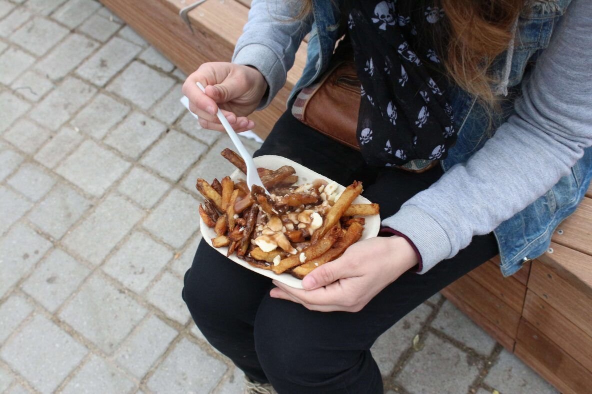 A lady sitting on a bench eating a poutine.