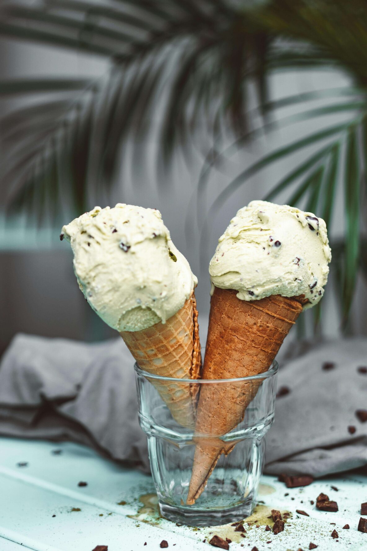 Two ice-cream cones sitting in a glass with chocolate around them.