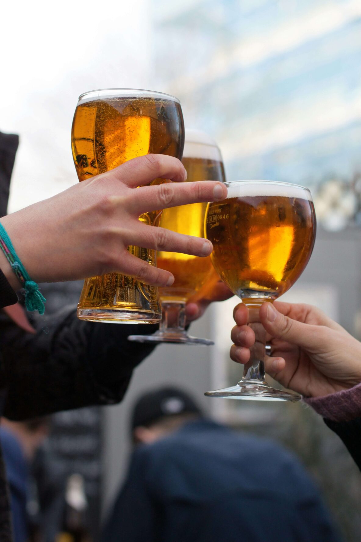 Three people bringing their beer glasses together in cheers.